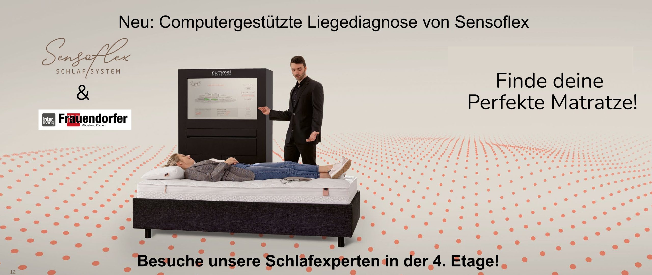 Ein Mann demonstriert einer Frau, die auf einem Bett in einem Ausstellungsraum mit deutschem Text liegt, ein Matratzen-Diagnosesystem.